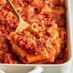 A spoonful of pasta al forno being lifted from a baking dish on a serving spoon.