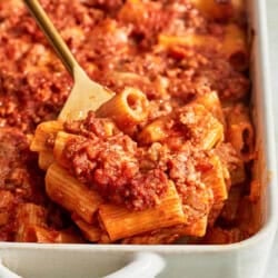 A spoonful of pasta al forno being lifted from a baking dish on a serving spoon.
