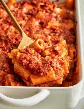 A spoonful of pasta al forno being lifted from a baking dish on a serving spoon.