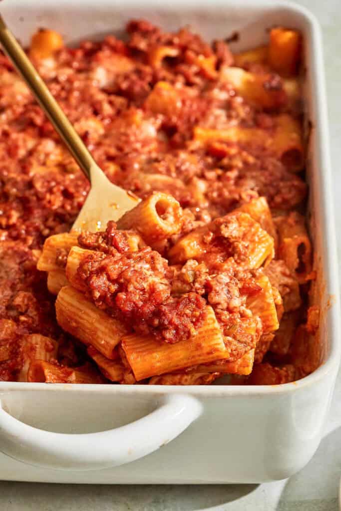 A spoonful of pasta al forno being lifted from a baking dish on a serving spoon.