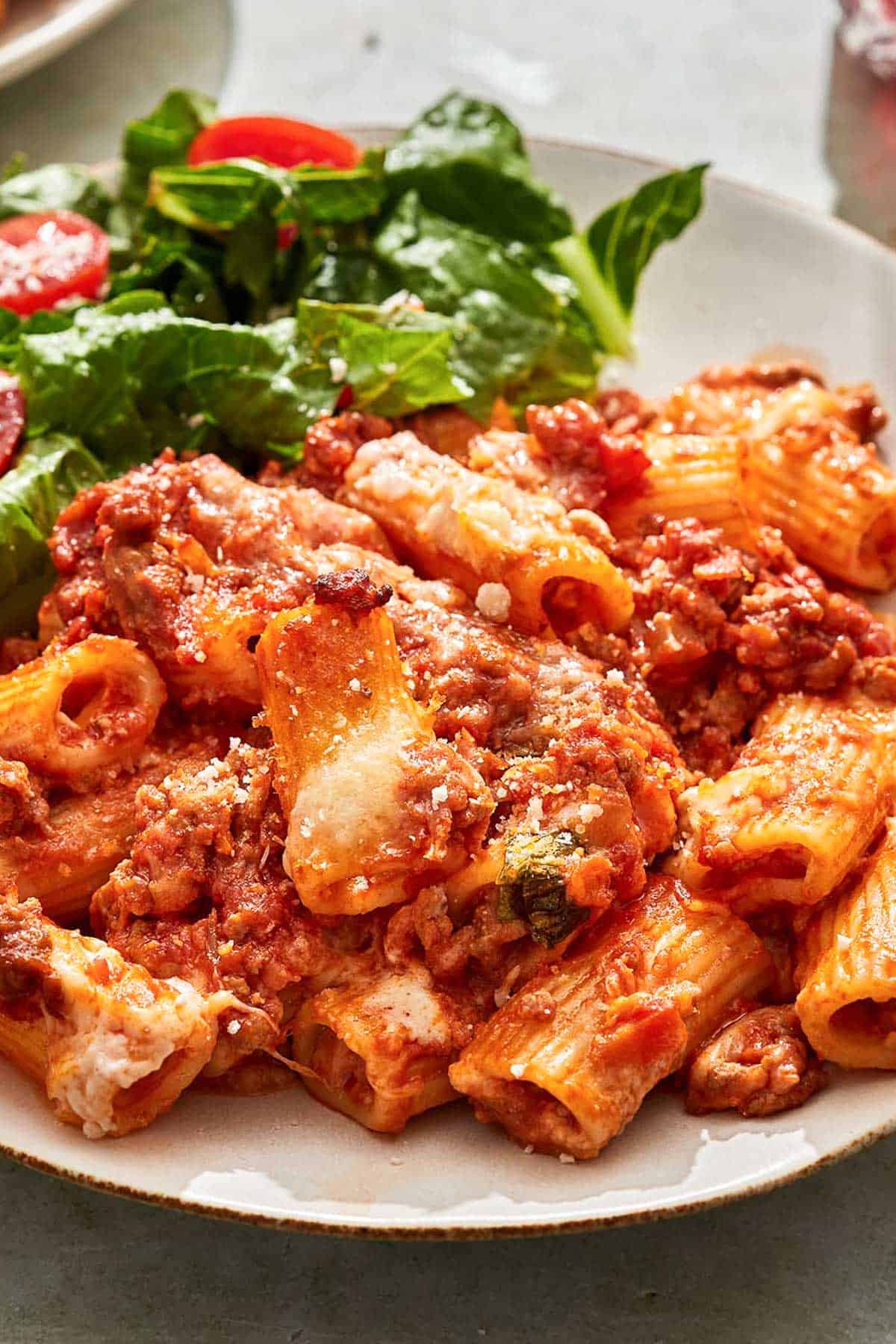 A serving of pasta al forno on a plate with a salad.