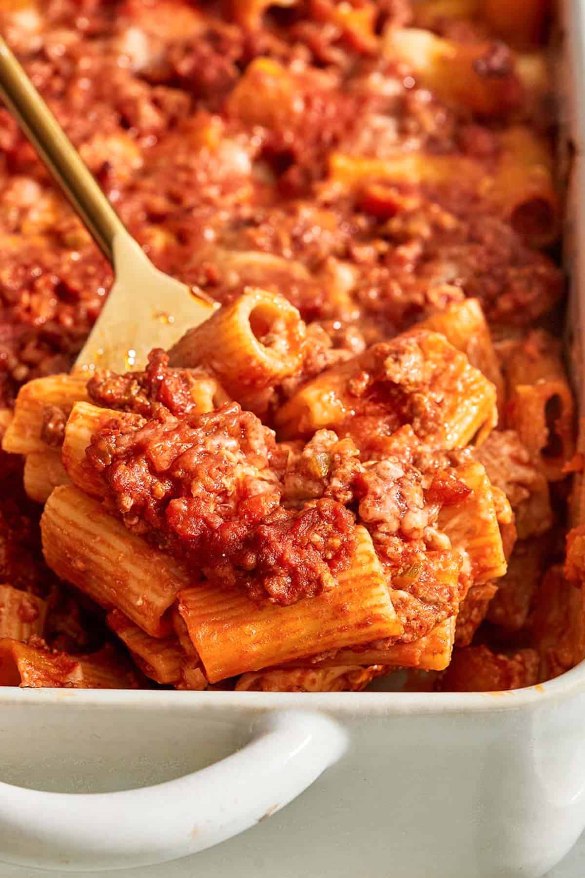 A spoonful of pasta al forno being lifted from a baking dish on a serving spoon.
