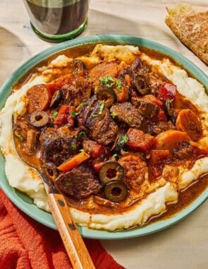 Daube provencal in a bowl with a fork next to a glass of red wine and a slice of crusty bread.