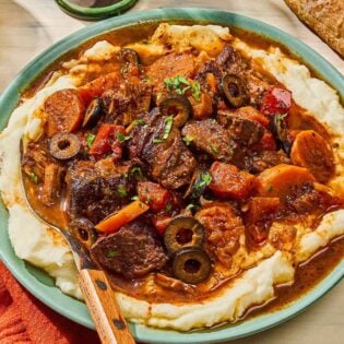 Daube provencal in a bowl with a fork next to a glass of red wine and a slice of crusty bread.