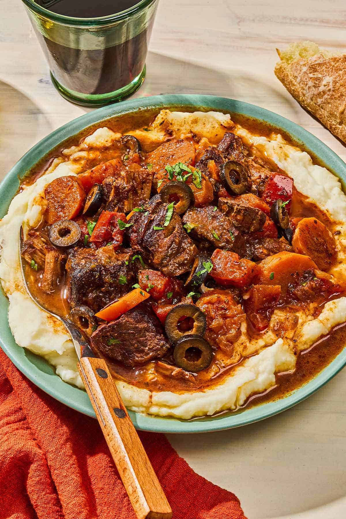 Daube provencal in a bowl with a fork next to a glass of red wine and a slice of crusty bread.
