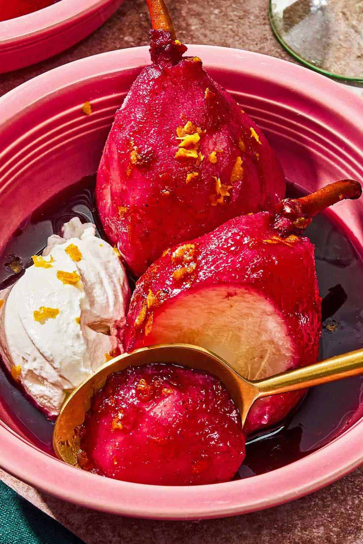 Poached pears in a bowl with whipped cream and a spoon.
