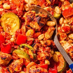 Sheet pan chicken and vegetables in a bowl with a spoon.