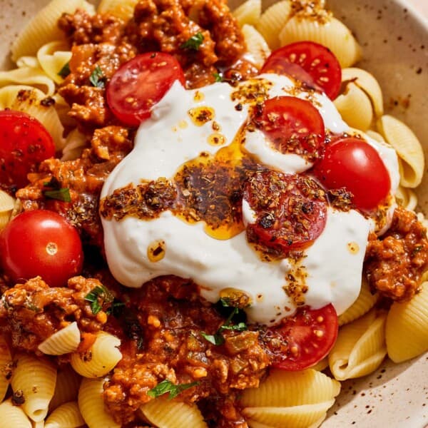 Turkish pasta topped with a meat sauce, cherry tomatoes, yogurt sauce and spiced oil in a bowl.