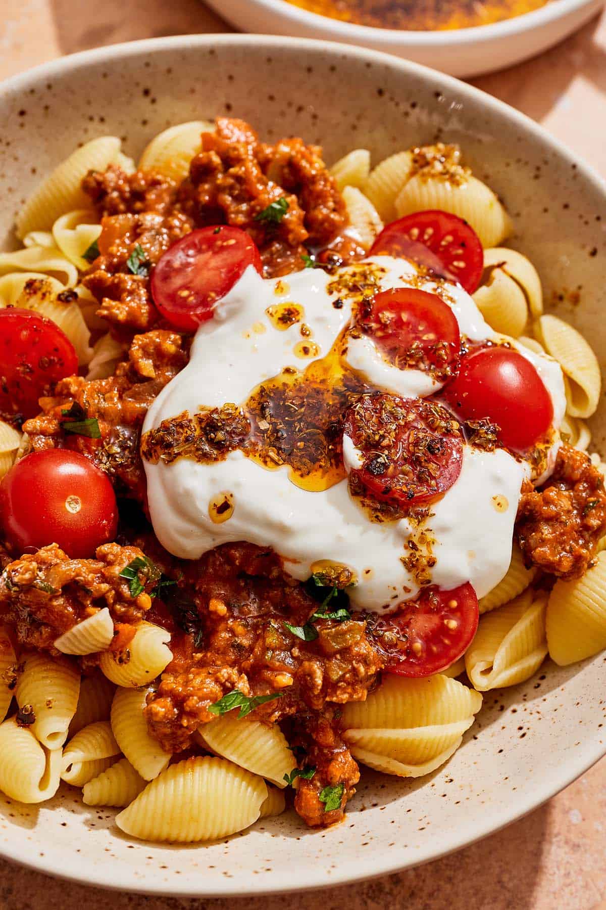 Turkish pasta topped with a meat sauce, cherry tomatoes, yogurt sauce and spiced oil in a bowl.