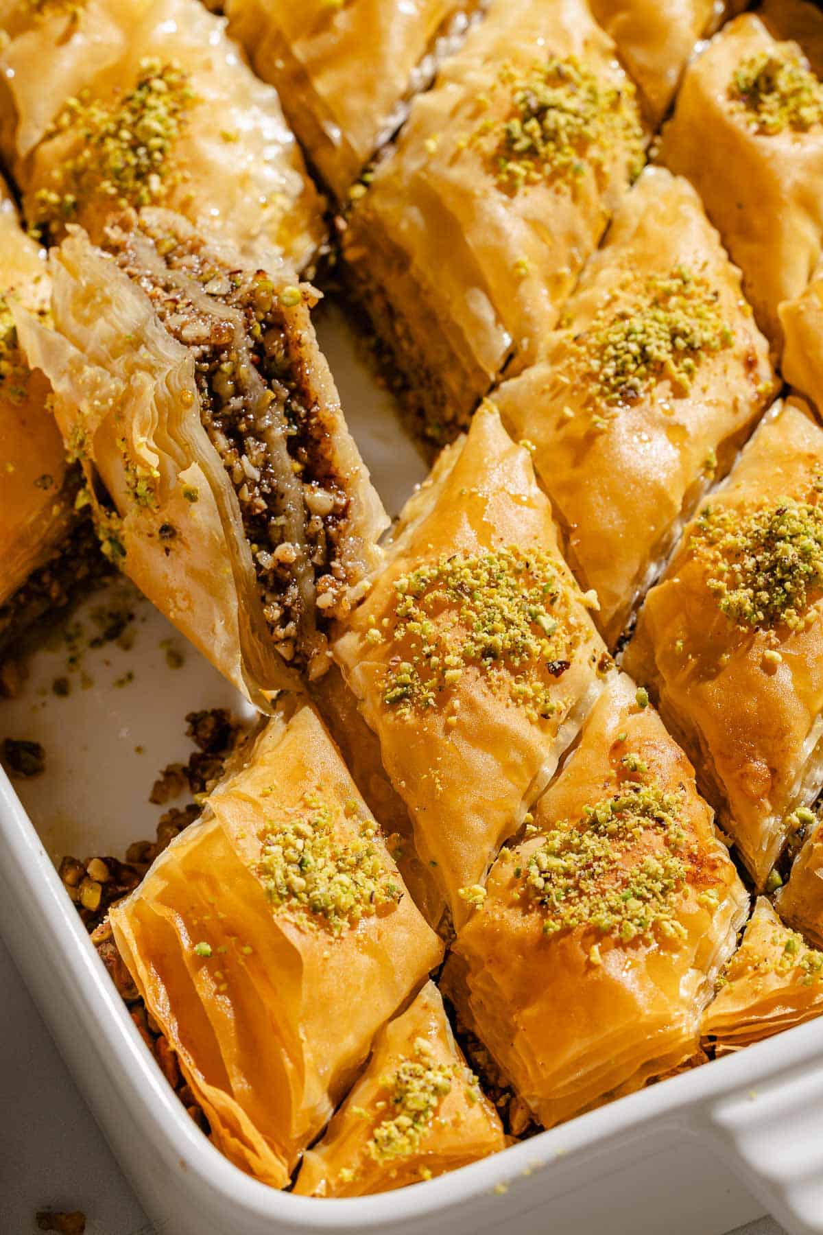 A slice of baklava being lifted out of the baking dish with the rest of the baklava.