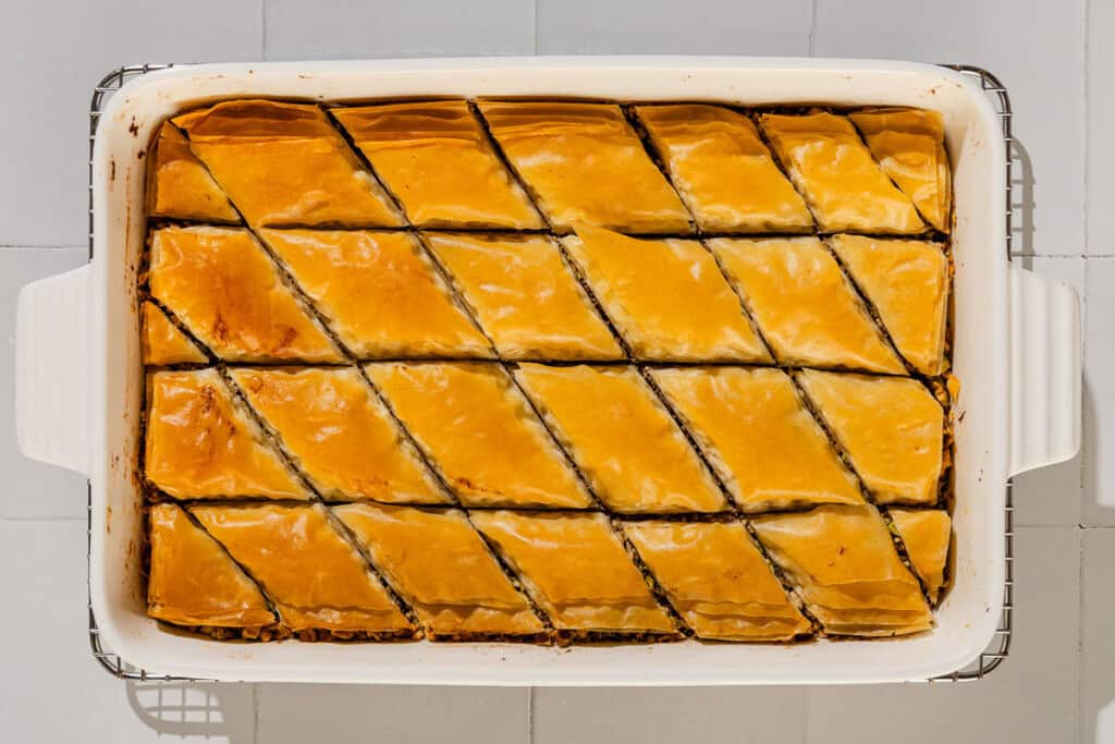 Sliced baklava in a baking dish cooling on a wire rack.