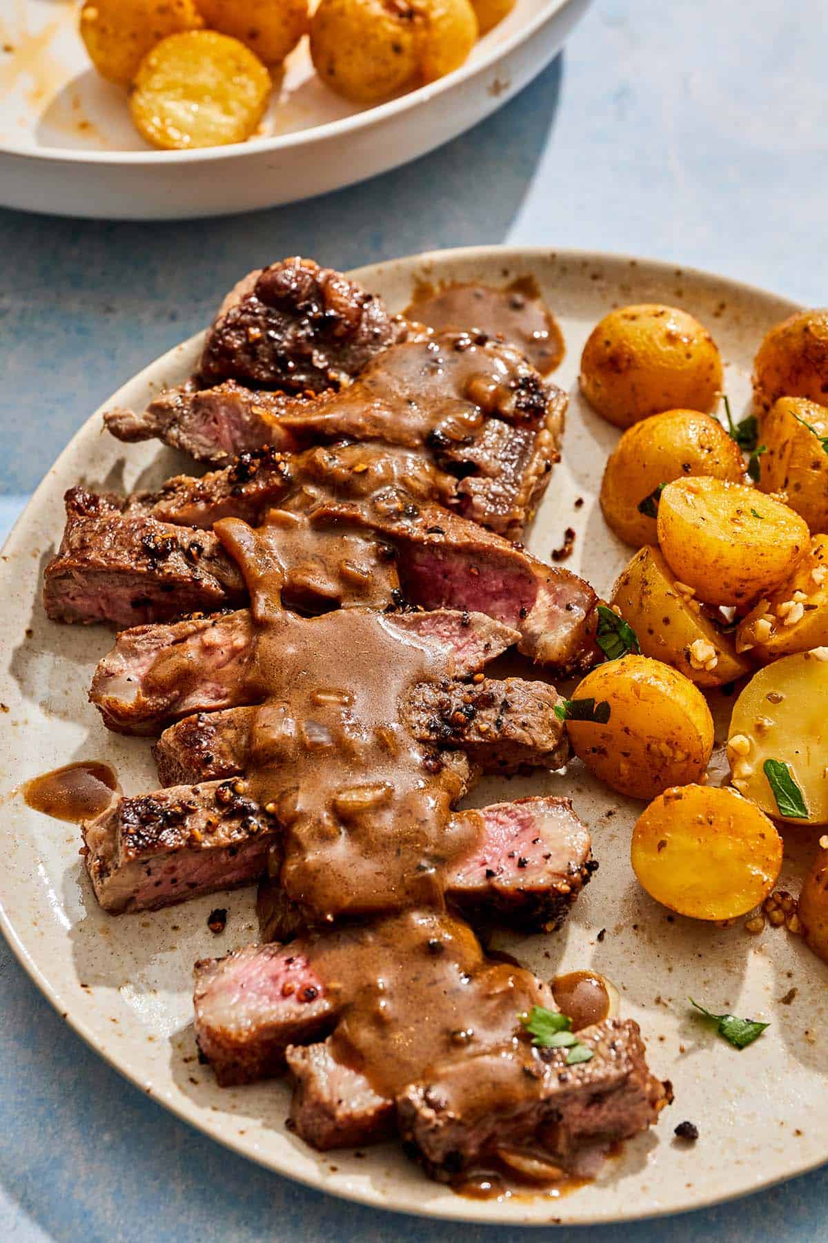 A serving of steak au poivre topped with sauce on a plate with potatoes.