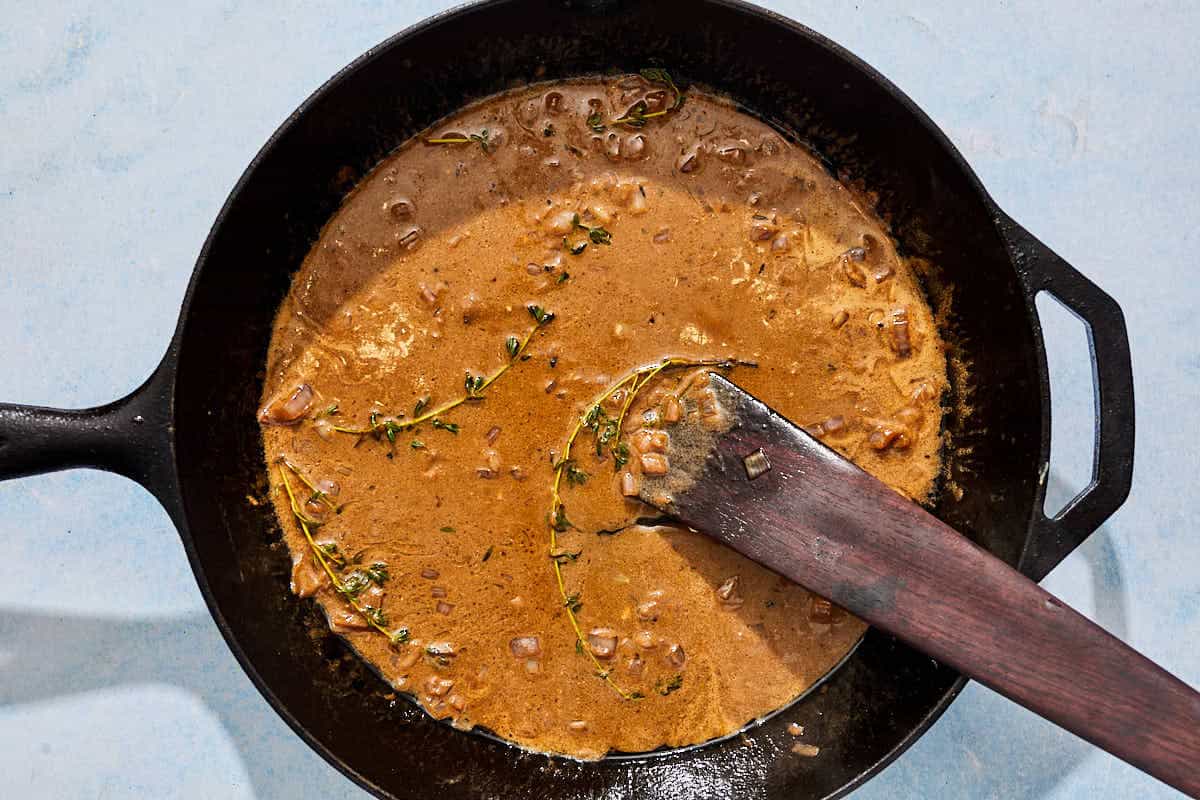 The pan sauce for the steak au poivre in a cast iron skillet with a wooden spatula.