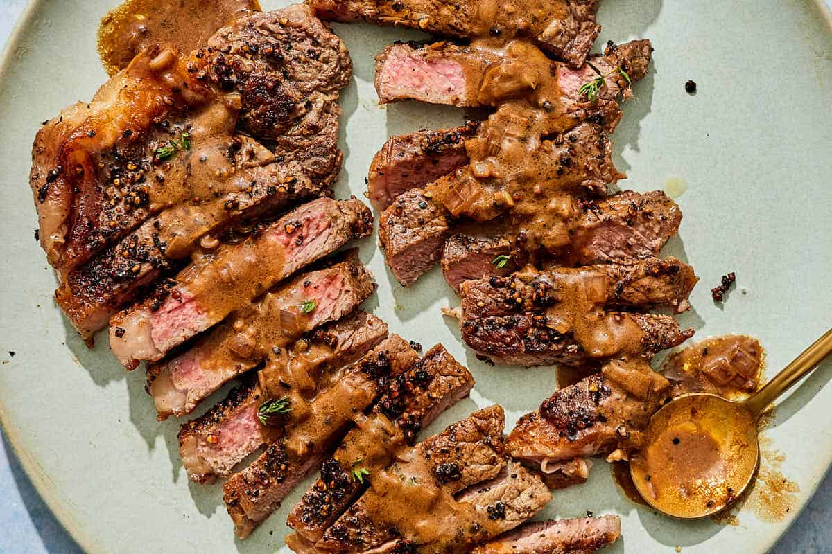 The sliced steak au poivre topped with pan sauce on a platter with a spoon.