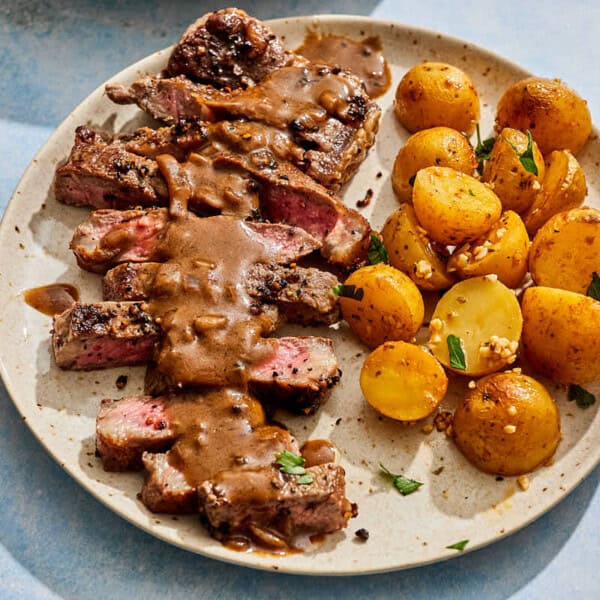 A serving of steak au poivre topped with sauce on a plate with potatoes.