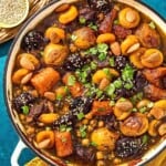 The beef tagine in a skillet next to bowls of sesame seeds and almonds.