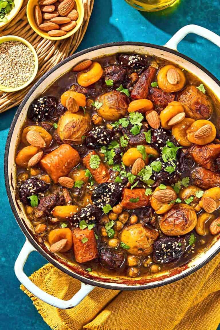 The beef tagine in a skillet next to bowls of sesame seeds and almonds.
