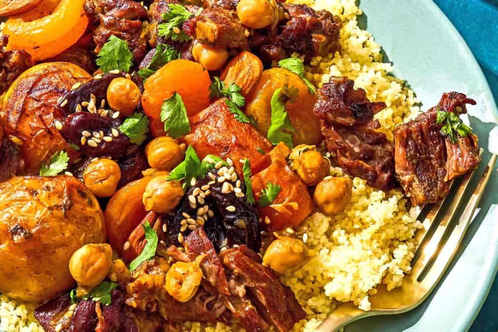 A serving of beef tagine over couscous in a bowl with a fork.