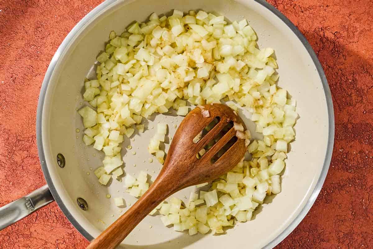 The onion for the chickpea skillet being softened in a skillet with a wooden spoon.