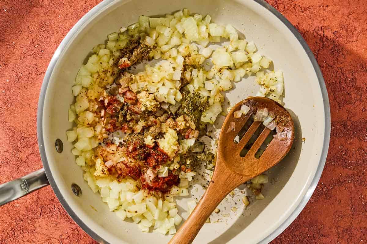 The onions for the chickpea skillet being sautéed with the spices in a skillet with a wooden spoon.