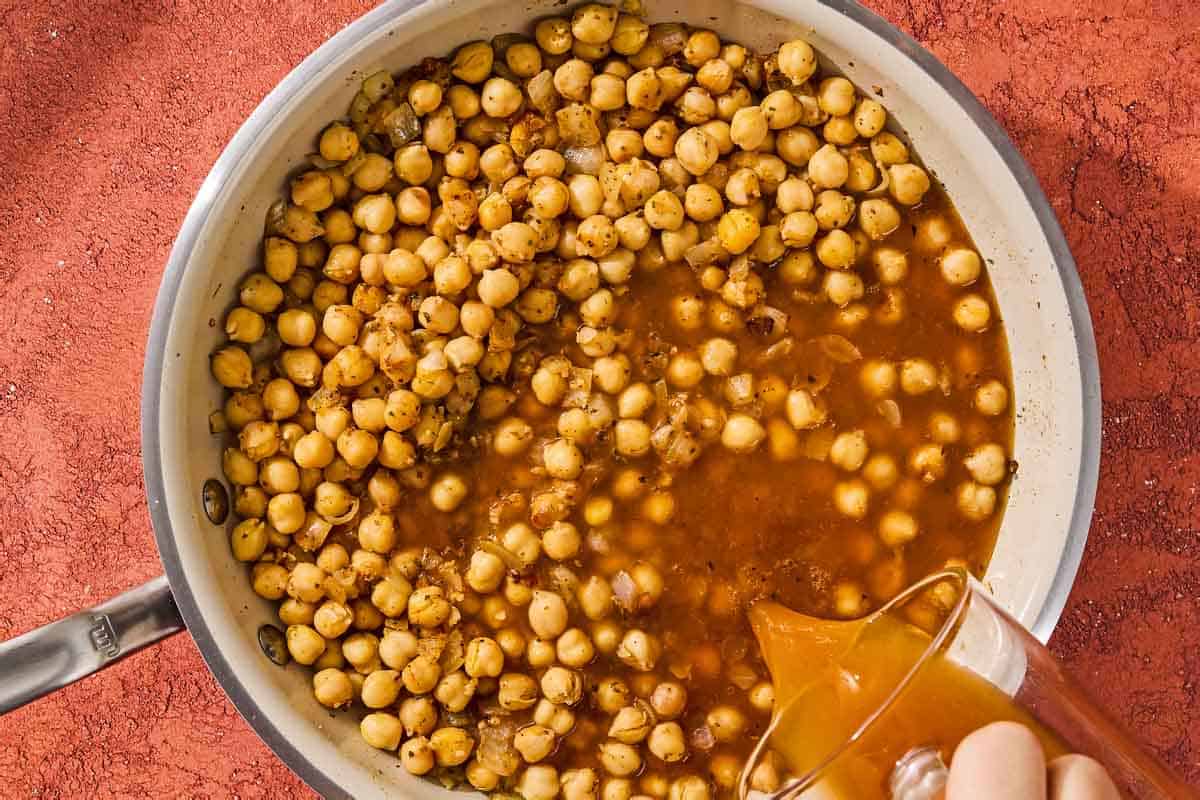 The broth for the chickpea skillet being added to the chickpeas in the skillet.