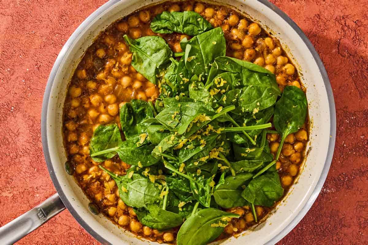 The spinach for the chickpea skillet being wilted in the skillet as the other ingredients simmer.