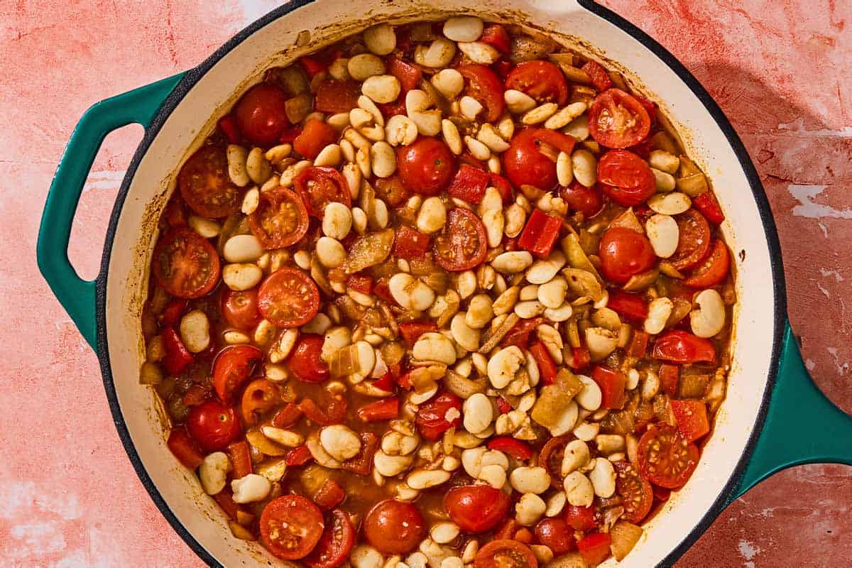 The broth, cherry tomatoes, beans and aromatics simmering together in a skillet.