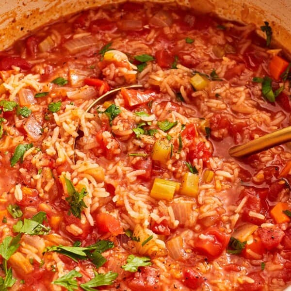 Tomato rice soup garnished with parsley in a large pot with a ladle.