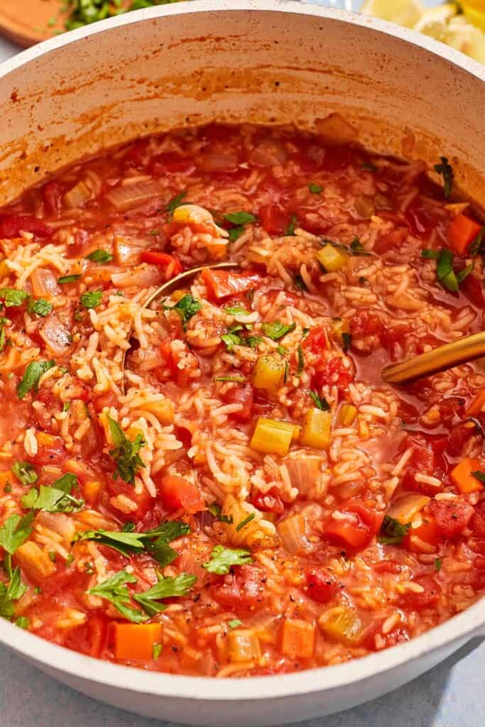 Tomato rice soup garnished with parsley in a large pot with a ladle.