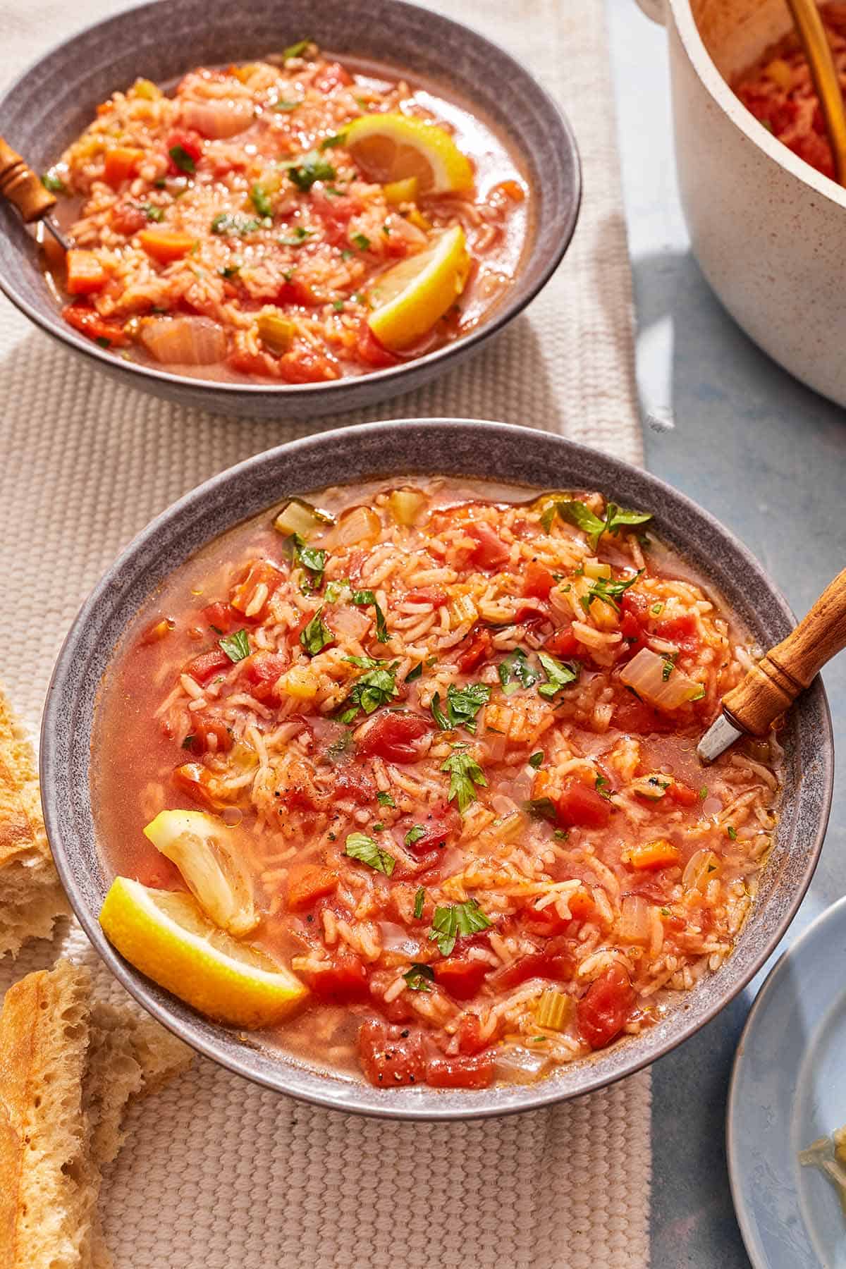 Two bowls of tomato rice soup with lemon wedges and spoons.