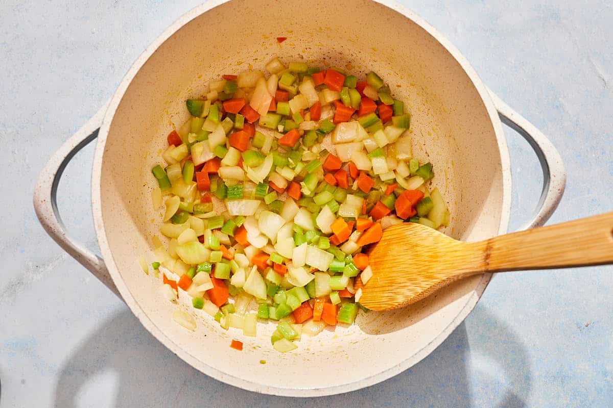 The vegetables for the tomato rice soup being sautéed in a pot with a wooden spoon.