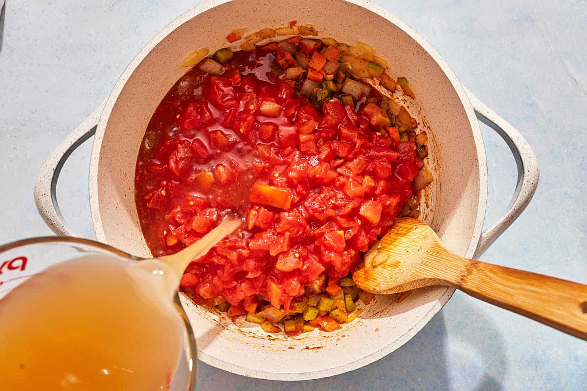 The tomatoes and broth for the tomato rice soup being added to the pot with the vegetables.