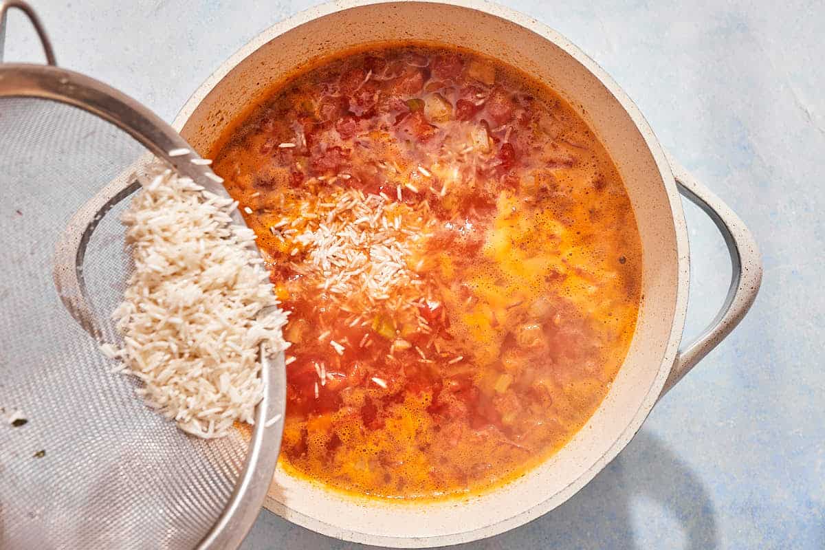 The uncooked rice being added to the tomato rice soup.